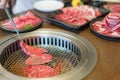 Close-up shot of a woman\'s hand tongs wagyu beef on a plate to grill in a charcoal grill. at a Japanese restaurant