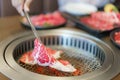 Close-up shot of a woman\'s hand tongs wagyu beef on a plate to grill in a charcoal grill. at a Japanese restaurant