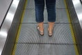 Close-up shot of the woman`s legs standing on metal escalator, back view