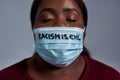 Close up shot of young african american woman wearing protective face mask with Racism is evil text posing with eyes Royalty Free Stock Photo