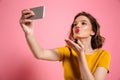 Close-up shot of young attractive woman with bright makeup sending air kiss while taking selfie on mobile phone Royalty Free Stock Photo