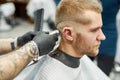 Close up shot of a young handsome caucasian man getting haircut, visiting barbershop. Barber using professional electric Royalty Free Stock Photo