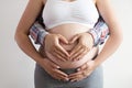 Close up shot of young man hugging his pregnant wife from behind, forming a heart shape with his hands over isolated white Royalty Free Stock Photo