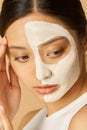 Close up shot of young woman with facial mask applied on half of her face receiving spa treatments, posing for camera