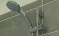 Close up of a shower head and a chrome adjustment bar in the shower enclosure of a grey tiled bathroom