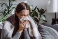 Close up of sick woman sitting on sofa freezing blowing running nose got fever caught cold sneezing in tissue, ill brunette girl Royalty Free Stock Photo