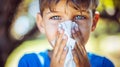 Close up of a sick young boy blowing his nose into a tissue, healthcare and illness concept Royalty Free Stock Photo