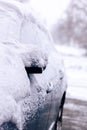 A close up of a side mirror of a blue car covered in white snow during winter parked on a driveway. The driver will have to clear Royalty Free Stock Photo
