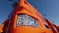 Close up of the side part of the truck body of red color and front headlight on blue clear sky background. Stock footage