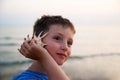 Close up side portrait of a beautiful young boy on holiday holding a sea shell to his ear and smiling, listening to the Royalty Free Stock Photo