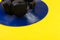 Black headphones lie on a blue vinyl record on a yellow background, side view Royalty Free Stock Photo