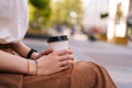 Close up side view cropped shot of unrecognizable elegant lady in casual clothes holding in hands paper cup with Royalty Free Stock Photo