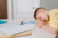 Close up side view of exhausted pupil boy sitting at home or classroom lying on desk filled with books training material Royalty Free Stock Photo