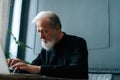 Close-up side view of focused bearded senior aged businessman working on laptop at workplace in dark home office room. Royalty Free Stock Photo