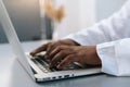 Close-up side view hands of unrecognizable African-American male doctor wearing white coat working typing on laptop Royalty Free Stock Photo