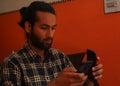 Close-up side view of a handsome bearded man with hair bun, holding two phones - Stock Photo Royalty Free Stock Photo