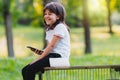 Close up side view photo of a joyful girl sitting on a bench with her legs dangling holding the smart phone in one hand
