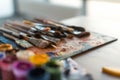 Close-up side view picture of a wooden paintbrush collection lying on old palette and gouache set in the workroom with