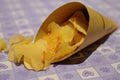 Close up side view of potato crisps in a paper cone on a table with a purple decorated table cloth.