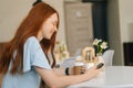 Close-up side view of smiling young woman using smartphone texting message and drinking hot coffee sitting at desk in Royalty Free Stock Photo