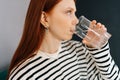 Close-up side view of thirsty redhead female holding glass, drinking still water enjoy natural aqua at home, preventing Royalty Free Stock Photo