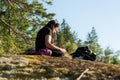 Close up side view of woman looking into mobile, sitting and relaxing warm evening Sunset on edge of pine tree forest.