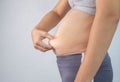 Close-up side view of woman`s hand pinching excessive belly fat on gray background. Woman fat belly. Obesity and