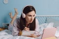 Young pretty calm brunette millennial woman in headphones lying on bed, watches webinar or lecture using digital tablet Royalty Free Stock Photo