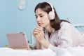 Young pretty calm brunette millennial woman in headphones lying on bed and watch webinar using digital tablet.