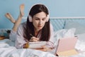 Young pretty calm brunette millennial woman in headphones lying on bed and watch webinar using digital tablet. Royalty Free Stock Photo