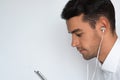 Close up sideways portrait of a handsome attractive young man in white shirt with earphones holding mobile phon