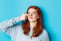 Close-up of silly redhead girl showing piggy nose, making funny grimaces and standing against blue background