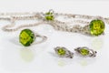 Close-up silver earrings, ring and pendant with peridot on background chain and ring on white acrylic desk.