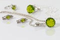 Close-up silver pendant, earrings with peridot on background chain and rings on white acrylic desk.