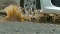 CLOSE UP: Silver vehicle drives into muddy puddle of water on black asphalt road Royalty Free Stock Photo