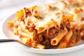 Close-up of a single baked ziti, cut in half, with a fork on a white plate, showcasing the layers of pasta, cheese, and meat