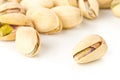 Close up of single pistachio in front of heap of salted, roasted green pistachio nuts snack over white background, healthy food