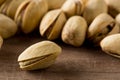 Close up of single pistachio in front of heap of salted, roasted green pistachio nuts snack over wooden background, healthy food