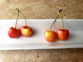 Close up on four paired up red and yellow cherries on a white plate