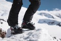 A close-up of a skier`s leg in ski boots without skis stands on a knoll of bliss against the background of mountains on