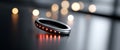Close-up of a sleek black smart ring with glowing red LED lights on a reflective surface with blurred warm bokeh lights in the Royalty Free Stock Photo