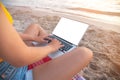 Close-up of a slender young woman on the beach at the sunset time by the sea works on her laptop holding him on her lap Royalty Free Stock Photo