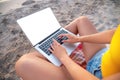 Close-up of a slender young woman on the beach at the sunset time by the sea works on her laptop holding him on her lap Royalty Free Stock Photo