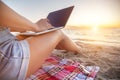 Close-up of a slender young woman on the beach at the sunset time by the sea works on her laptop holding him on her lap Royalty Free Stock Photo