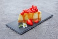 Close-up slice of delicious homemade cheesecake with fresh strawberries, spring flowers and caramel sauce on black slate board Royalty Free Stock Photo