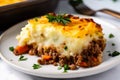 Close-up of a slice of piping hot Shepherds Pie on a white plate with a dollop of sour cream on top