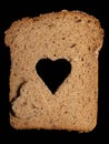 Close-up of a slice of whole wheat bread lying on a dark background. A heart is cut into the bread in the middle. The cut out Royalty Free Stock Photo