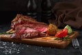 Close up sliced medium rare grilled beef steak with corn and tomato, pepper and rosemary on meat cutting board on dark Royalty Free Stock Photo