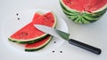 Close-up slices of fresh ripe red watermelon on a plate with a knife on the table on a white background, half of a watermelon. Royalty Free Stock Photo