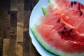 Close-up slices of watermelon on a white plate on a wooden table with copy space. Ripe red watermelon cut into slices on a wooden